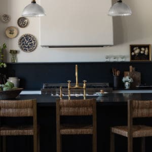 kitchen scene with wicker barstools in front of an all black island, tongue and groove ceiling with plaster hood