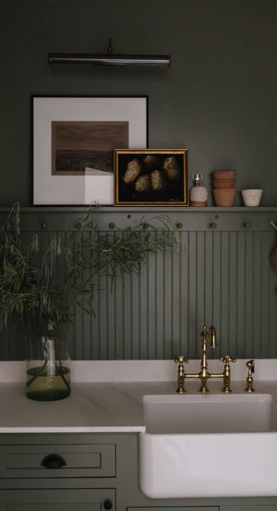 green cabinets and walls with a peg rail and marble counters with white farmhouse sink