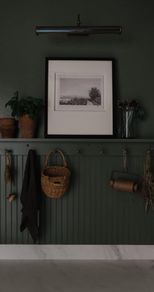 beadboard wall with a pegrail above in a green paint color with decor hanging off the pegrail and artwork and vases on the shelf
