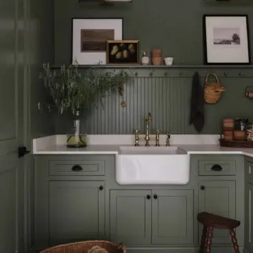 green cabinets and walls with a peg rail and marble counters with white farmhouse sink