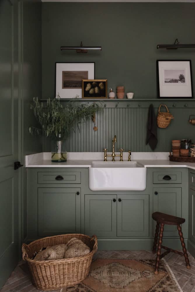 green cabinets and walls with a peg rail and marble counters with white farmhouse sink