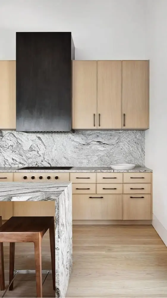 modern wood tone kitchen with a black metal hood with black and white swirled granite countertops