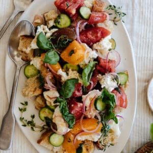 panzanella salad on a white platter on a linen tablecloth with a fork and knife leaning on the platter