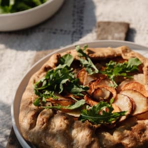 potato galette on a white plate on top of a rustic wood cutting board with a salad in the background