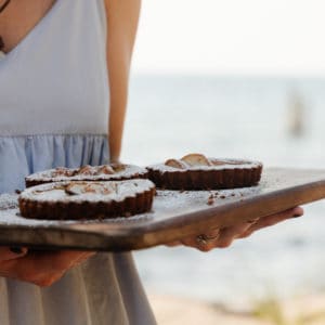 woman in a dress holding a rustic wood tray with 3 small pear tarts with powdered sugar dusted on top