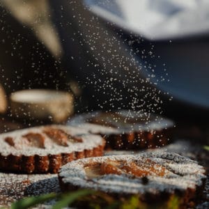 powdered sugar being dusted on top of 3 small pear tarts on top of a rustic wood cutting board