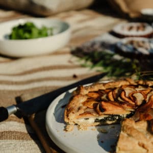 potato galette on a white plate on top of a rustic wood cutting board with a salad in the background