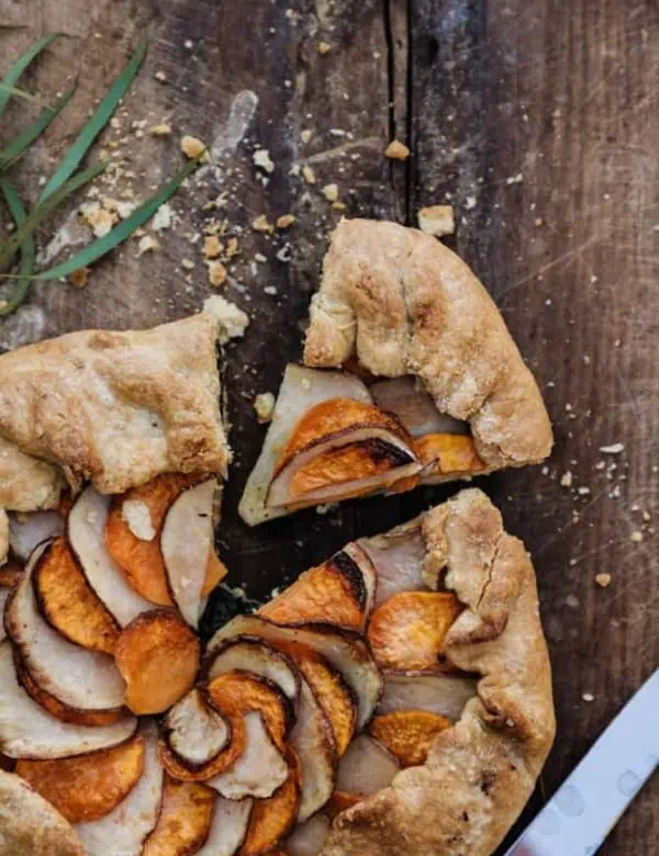 top view of potato galette with one slice cut out on top of a rustic wood cutting board