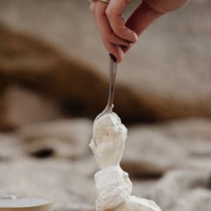 womans hand holding a spoon vertically above a pear tart with whipped cream being dolloped on top