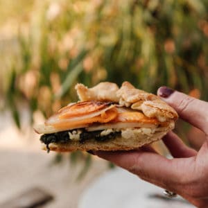 womans hand holding a slice of potato and kale galette with out of focus background