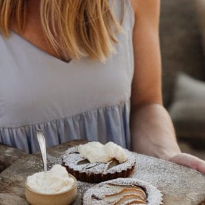 woman holding a rustic cutting board with 2 pear tarts and a bowl of whipped cream