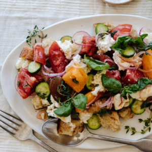 fork and spoon laying on a white platter filled with panzanella salad