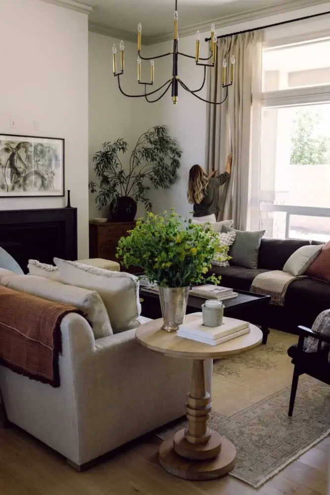 side view into a living room with 2 sofas facing each other, greenery on side tables, and a large chandelier in the center of the room