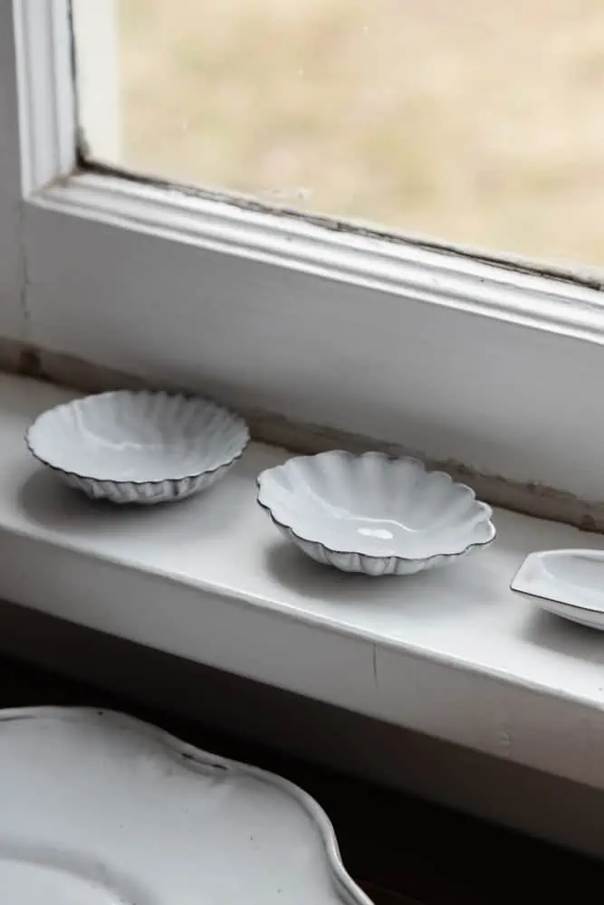 scalloped white french ceramic dishes on a window ledge