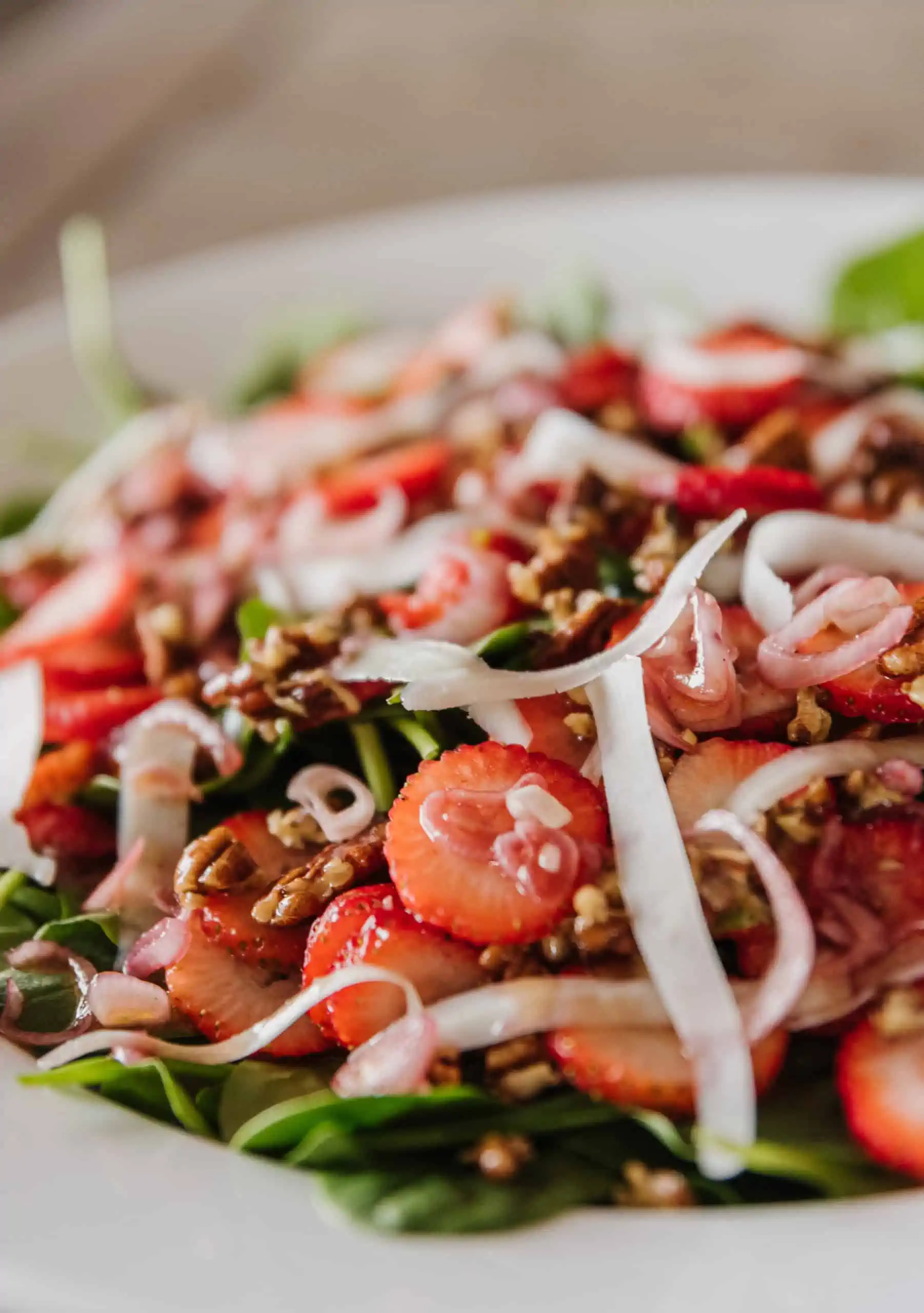 close up view of a strawberry spinach salad featuring shaved goat cheese and candied pecans
