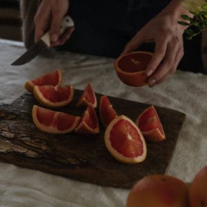 linen covered table with an antique wood cutting board with a woman's hand cutting grapefruits
