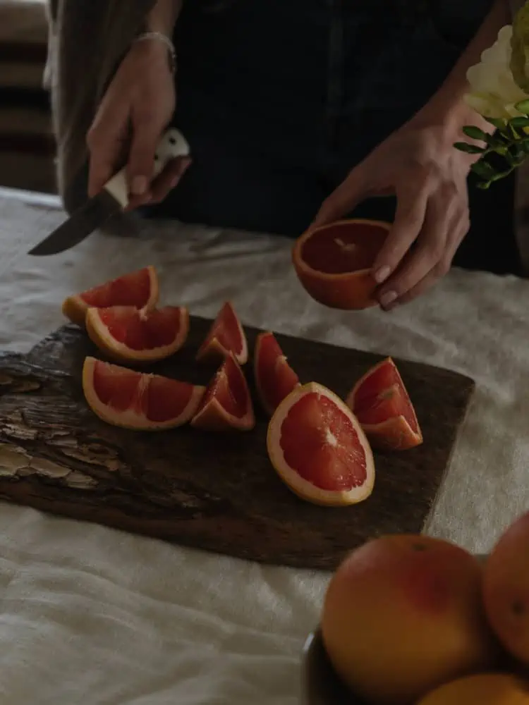 linen covered table with an antique wood cutting board with a woman's hand cutting grapefruits