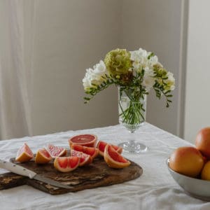 linen covered table with glass vase of flowers in the corner and an antique wood cutting board with cut grapefruits
