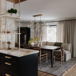 mable and brass shelving on top of a black cabinet with a marble countertop. Modern dining room table and glass and brass bubble light fixture centered above the table and a taupe linen sofa as bench seating for the table.