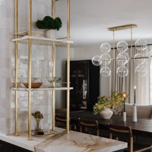 mable and brass shelving on top of a black cabinet with a marble countertop. Dining room table and glass and brass bubble light fixture centered above the table.