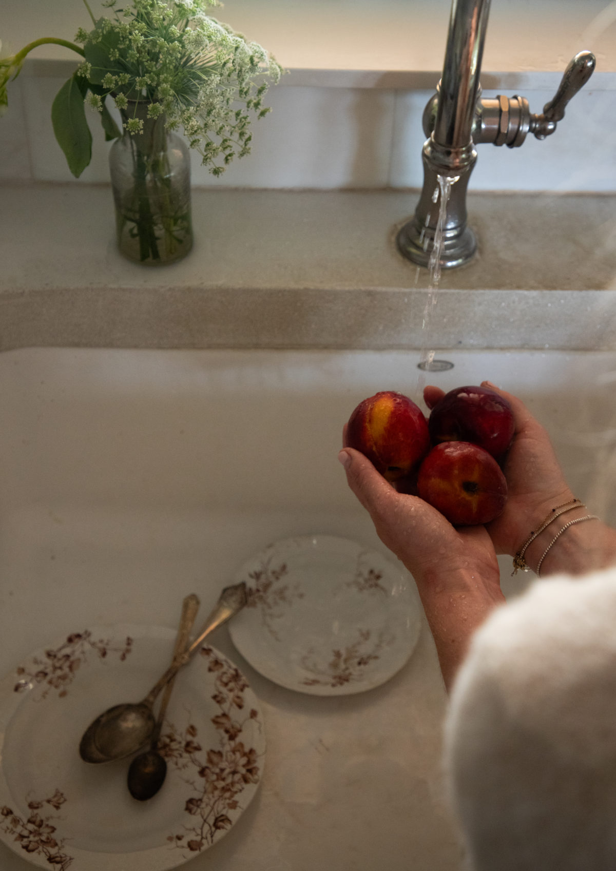 woman's hands holding 3 peaches above a sink with brown floral dishes in the sink below