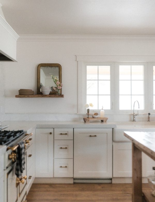 An open white kitchen with white concrete countertops and light filtering through the windows.