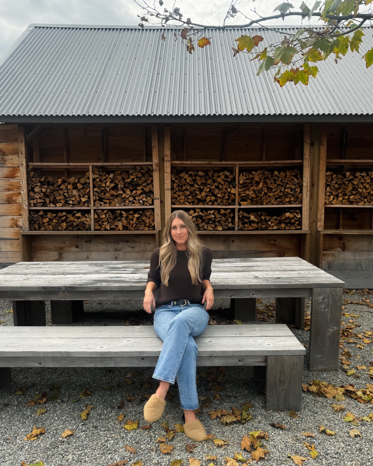 Chloe in Inness, New York, wearing Jenni Kayne, sitting on a picnic bench and surrounded by the stunning natural beauty of the area, offering a perfect blend of style and serene outdoor vibes.